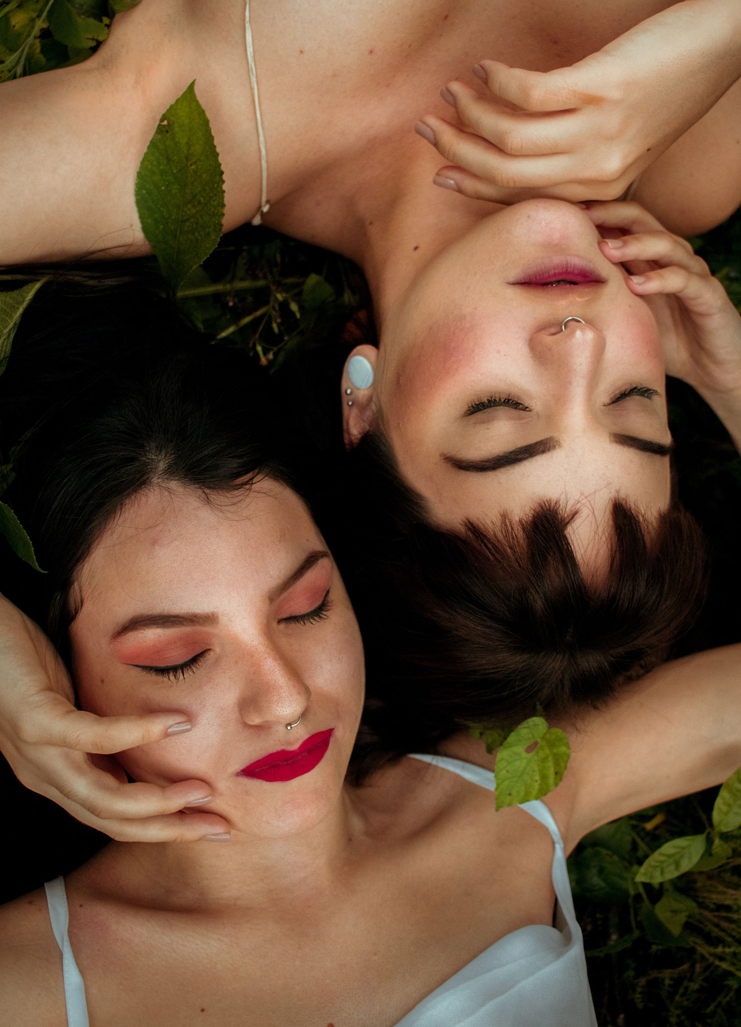 Two young women laying next to each other with pierced noses and ears